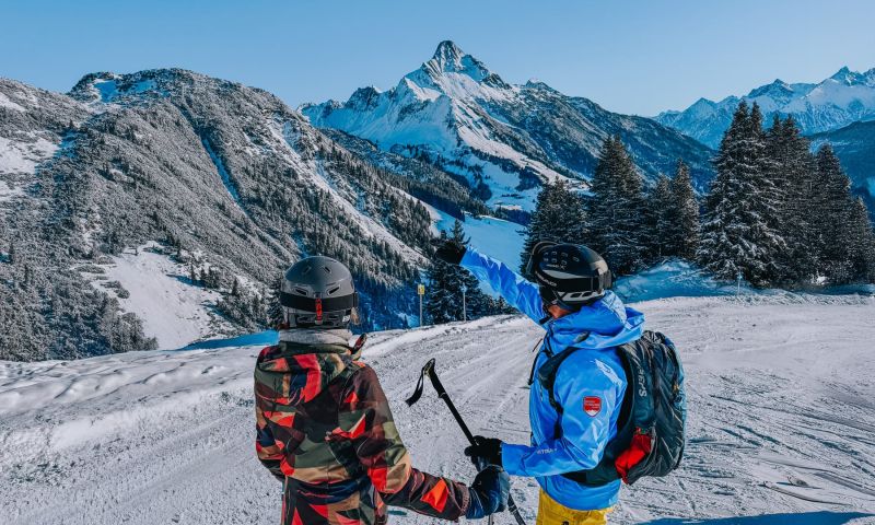 Familie beim Skifahren auf schneebedeckten Pisten in Warth-Schröcken am Arlberg mit klar blauem Himmel im Hintergrund, im größten Skigebiet Österreichs.